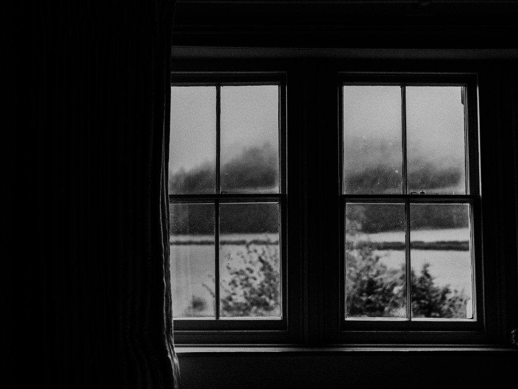 Snowy field through curtained window. Black and white photography.