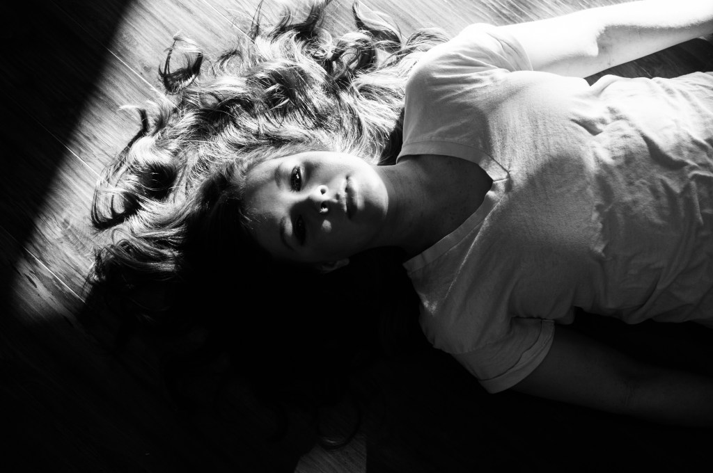 Black and white photo of girl lying in sunlight on the floor.